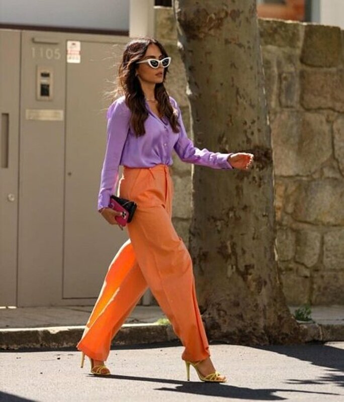 Fashionable woman in purple shirt and orange pants walking.