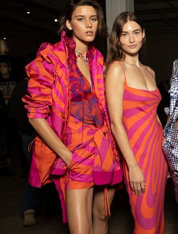 Three models in vibrant outfits walking down the runway at a fashion show.