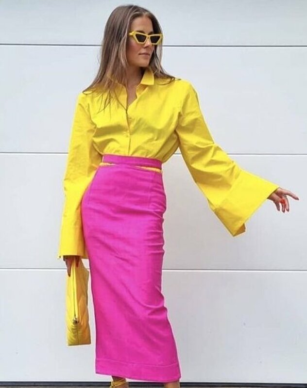A woman wearing a yellow shirt and pink skirt, looking stylish and confident.