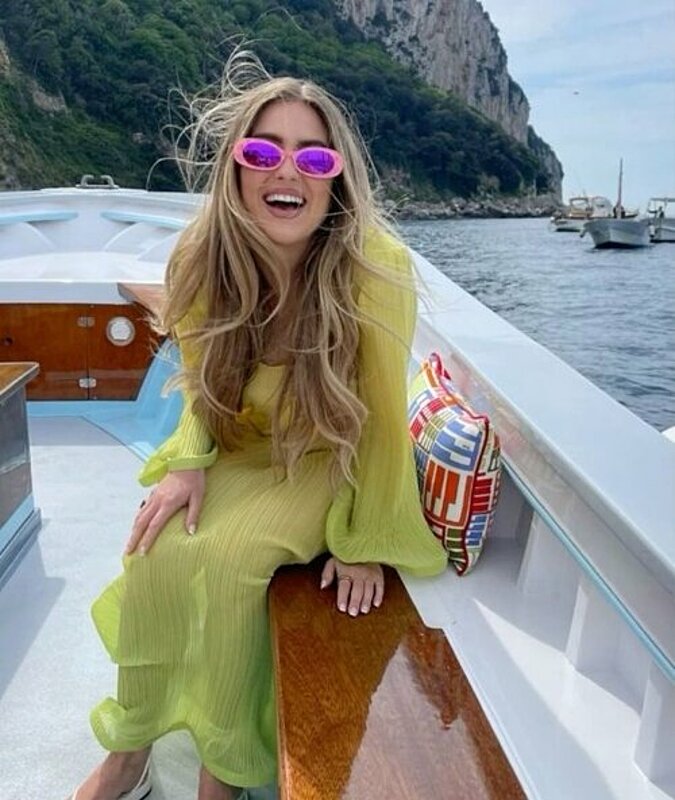A woman in a yellow dress and sunglasses enjoying a sunny day on a boat.