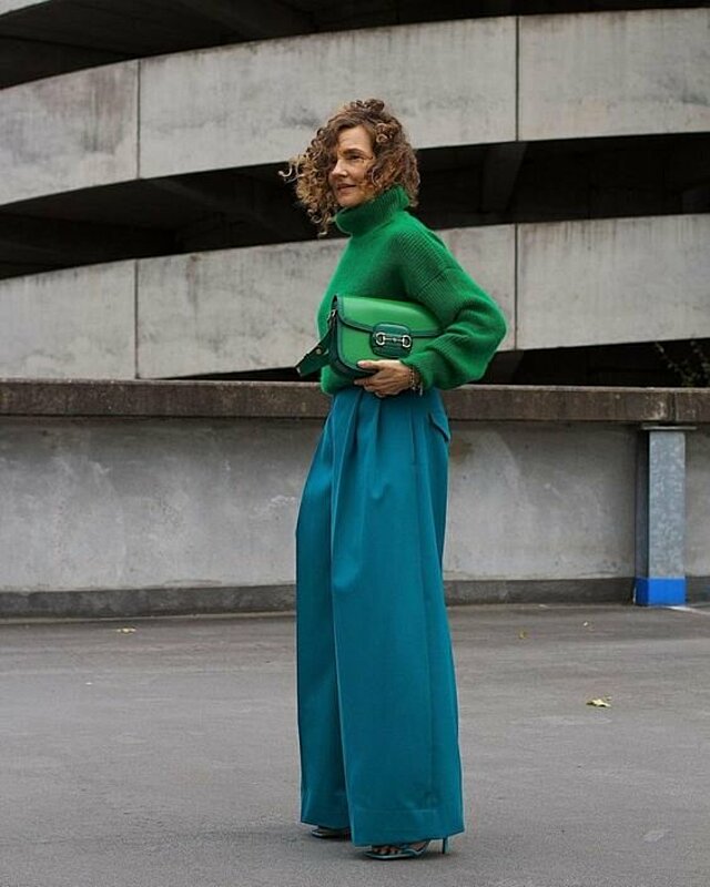 a woman in a green sweater and wide pants