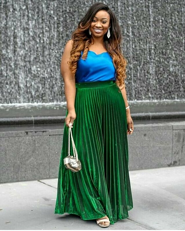 A stylish woman wearing a green pleated skirt and a blue top.