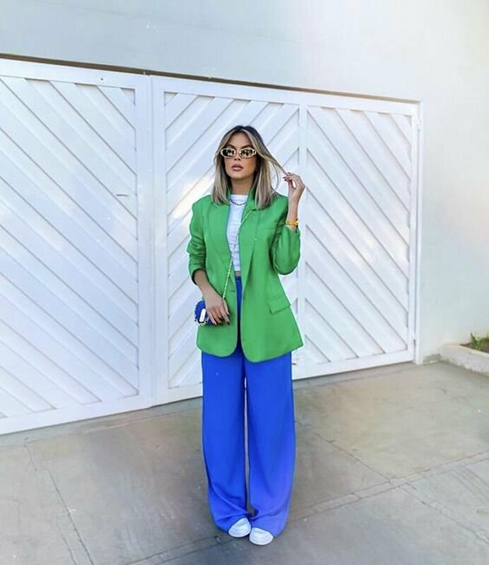 امرأة ترتدي بليزر أخضر وبنطال أزرق.