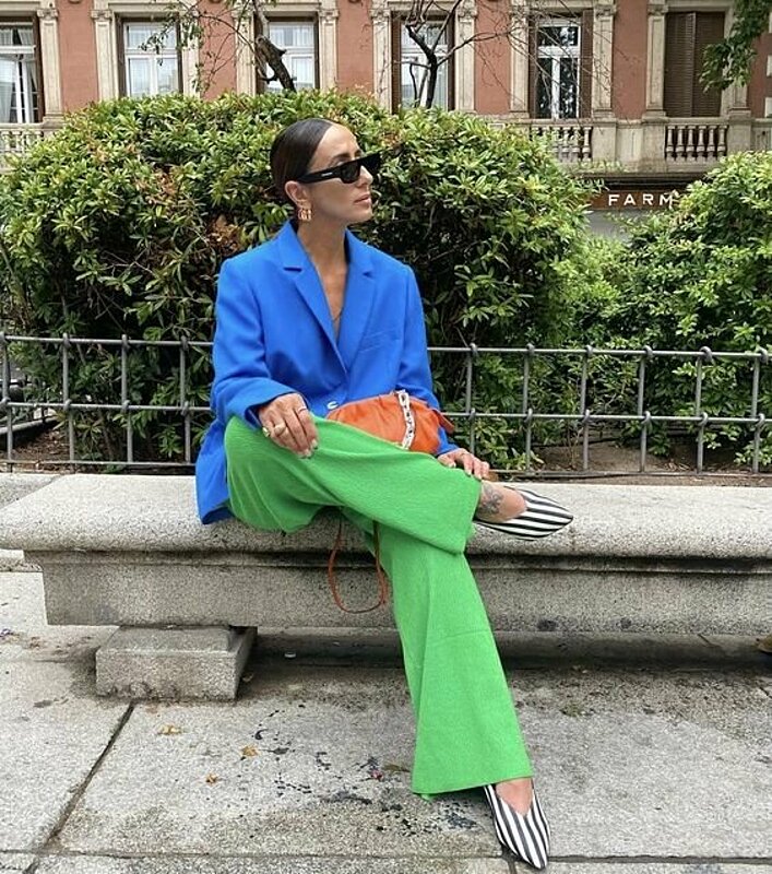 A woman in a vibrant blue suit and green pants sitting on a bench, enjoying a peaceful moment.